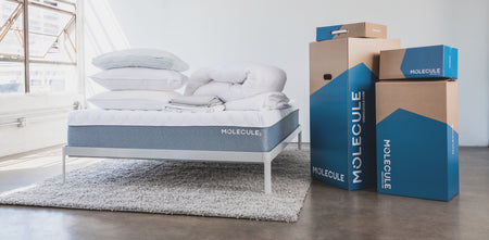 Molecule boxes adjacent to a bed frame that has a Molecule mattress, pillows, and bedding on top of it